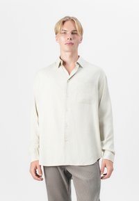 Hellbeige Langarmhemd aus strukturiertem Material, mit durchgehender Knopfleiste, spitzem Kragen und einer einzigen Brusttasche.