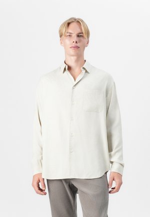 Light beige long-sleeve shirt in a textured material, featuring a button-up front, pointed collar, and a single chest pocket.
