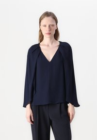 Blusa blu navy con scollo a V e maniche ampie. Realizzata in tessuto leggero, presenta eleganti dettagli drappeggiati vicino alle spalle.