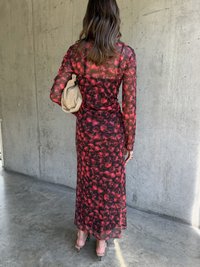 Gjennomsiktig langermet kjole med rødt blomstermønster, tettsittende silhuett og en flytende skjørt. Kombinert med en beige clutch og sandaler med rem.