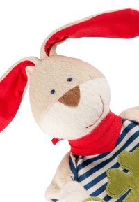 Soft beige bunny toy with large red ears, blue embroidered eyes, brown nose, red neck scarf, striped shirt, and green clover patch.
