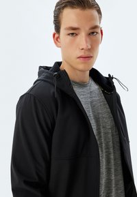 Sort zip-jakke med hætte, der har en blød foring, kombineret med en grå meleret t-shirt under. Glat, slidstærkt stof.