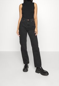 Black high-waisted jeans with a straight leg design, featuring front pockets and a button closure. Paired with a black sleeveless top and chunky black boots.