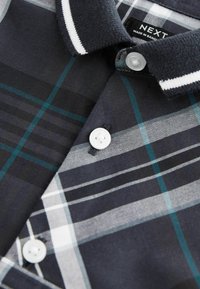 Polo shirt a quadri navy con accenti bianchi, chiusura con bottoni e colletto testurizzato. Presenta diverse tonalità di navy, teal e motivi grigi.