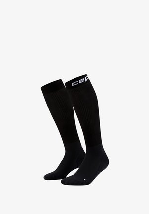 Paire de chaussettes de compression noires montantes jusqu'au genou, avec une texture côtelée et un logo blanc près du bord supérieur.