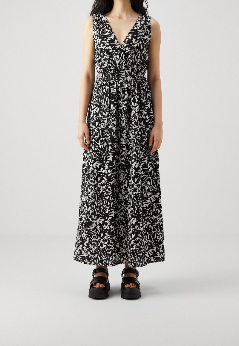 Robe maxi noire et blanche avec un décolleté en V, motif floral, taille cintrée et jupe fluide ; associée à des sandales noires épaisses.