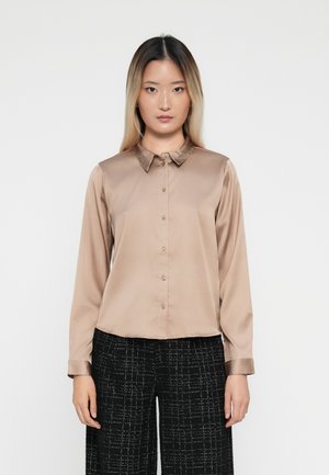 Beige satijnen overhemd met knopen, voorzien van een geribbelde kraag en lange mouwen, met een rechte snit en subtiele glans. Gdragend met gestructureerde zwarte broek.