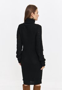 Czarna dzianinowa sukienka z wysokim kołnierzem i długimi rękawami w warkocz. Teksturowany materiał o dopasowanym kroju, sięgającym do kolan.