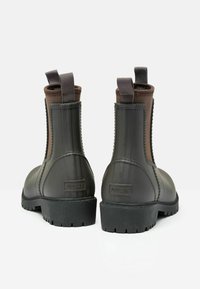 Brązowe gumowe botki Chelsea z teksturowanym wzorem, uchwytami do zakładania oraz solidną czarną podeszwą z widocznymi detalami bieżnika. Logo marki widoczne na pięcie.