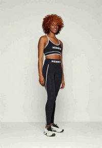 Svart träningsset med en kort topp och högmidjade leggings med vita sidoränder och "NEBBIA"-logotyp. Texturerat tyg, figurnära design.