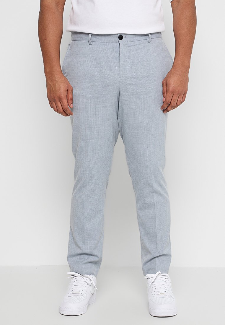 Jasnoszare, teksturowane chinosy o slim fit, z zapięciem na guzik i kieszeniami z przodu, w zestawieniu z białymi sneakersami.