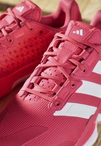 Pink athletic shoes with a breathable mesh upper, textured rubber sole, synthetic accents, and three white stripes on the side.