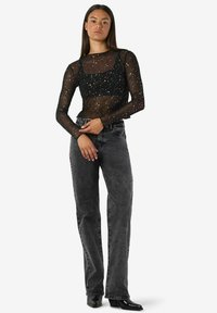 Črni prosojni dolgi rokavi s razpršenimi zlatimi pikami, v kombinaciji z visokim pasom in sivimi ravnimi hlačami. Hlače imajo klasičen dizajn s štirimi žepi.