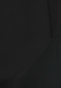 Gros plan sur un tissu noir aux textures variées et aux détails de couture subtils sur le côté droit.