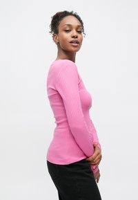 Eng anliegendes Langarmshirt aus weichem, rosa, geripptem Material mit rundem Ausschnitt und schmaler Passform, kombiniert mit dunklen schwarzen Hosen.