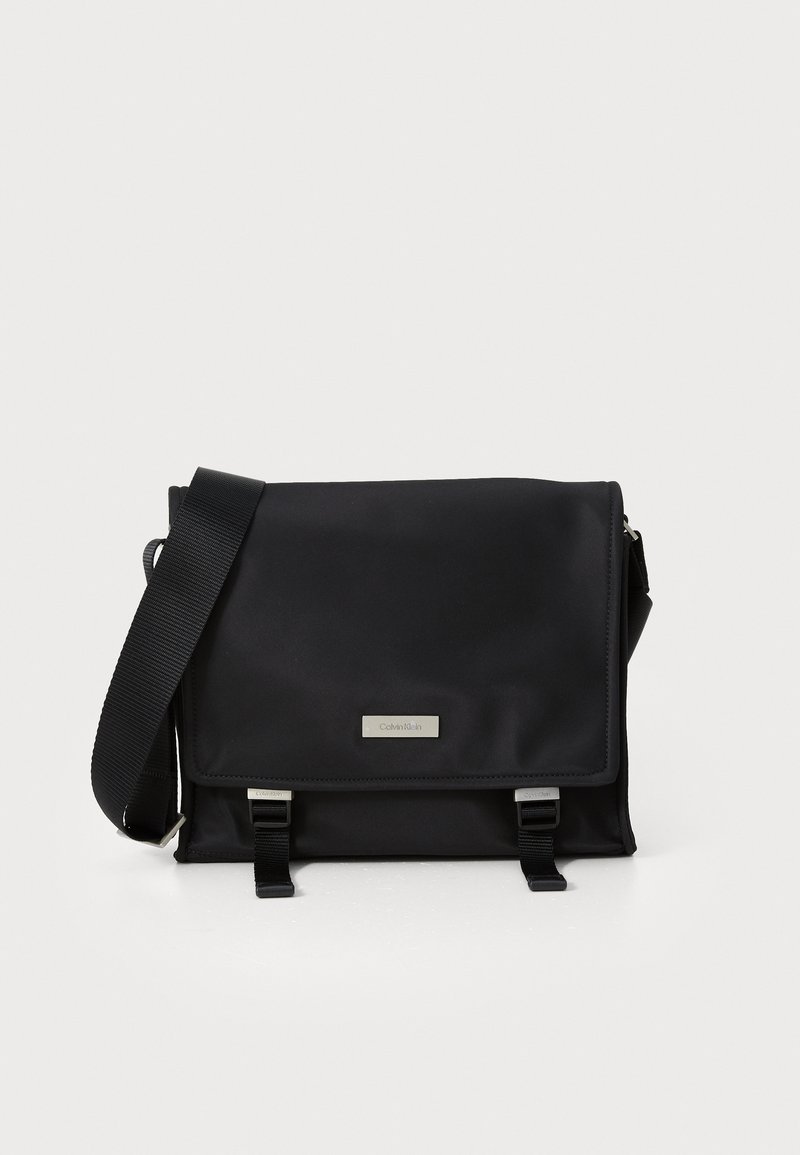 Borsa a tracolla nera realizzata in nylon liscio con chiusura a patta, hardware in argento e tracolla regolabile intrecciata. Caratterizzata da un'etichetta con logo e dettagli con fibbia.