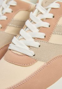 Jasnoróżowe i beżowe sneakersy z połączeniem gładkiego i teksturowanego zamszu, z białymi sznurowadłami i podwójnym przeszyciem.