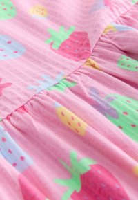 Rózsaszín anyag színes eper- és gyümölcsmintákkal, valamint összehúzott varrással, amely lágy redőket képez.