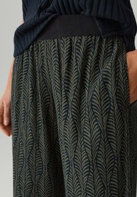 Pantaloni con motivo su base verde scuro e design a foglia blu navy. Presentano un elastico in vita nero e un tessuto morbido e strutturato.