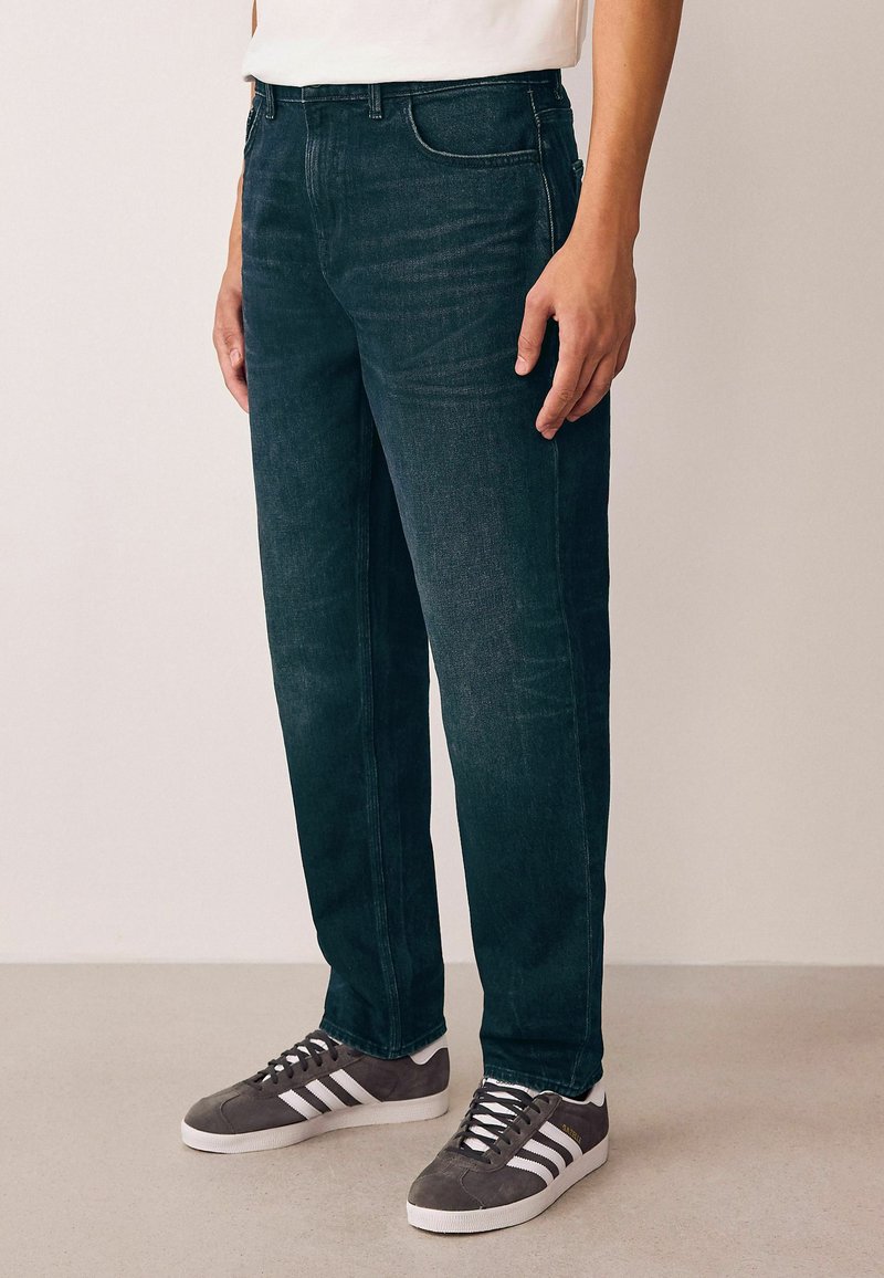 Jeans din denim de un verde închis, cu croi drept, având cinci buzunare și cusături în contrast, asortați cu adidași gri.