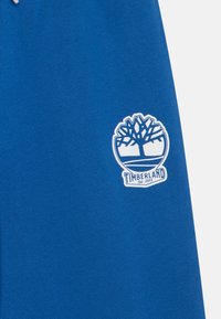 Blauwe katoenen shorts met een wit geborduurd Timberland-logo met een boomontwerp, met het jaartal 1973 onderaan. Eenvoudig detail.