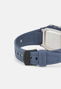 Casio digital watch with a rectangular silver stainless steel case, blue rubber strap, black buckle, and multiple adjustment holes.