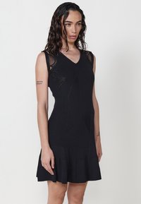 Schwarzes ärmelloses Kleid mit V-Ausschnitt, geripptem Textur und floralem Muster an den Schultern. Ausgestellter Saum am unteren Ende. Glatte Stoffoberfläche.