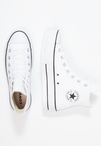 Bílé vysoké tenisky Converse mají plátěný svršek, černou logo nášivku a gumovou podrážku s černým lemem. Klasický design na šněrování.