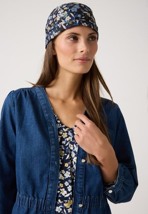 Jeansjacke mit tailliertem Schnitt und Knopfverschluss, über einem blumenbedruckten Oberteil in Marineblau getragen, das gelbe und weiße Blumen aufweist.