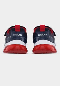 Ζεύγος αθλητικών παπουτσιών Geox σε σκούρο μπλε και κόκκινο, εμφανιζόμενα από πίσω, με λευκές μεσαίες σόλες και κόκκινες εξωτερικές σόλες σε λευκό φόντο.