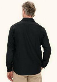 Black long-sleeve shirt with a collar, buttoned cuffs, and a textured fabric. Back view shows a straight hem and tailored fit.