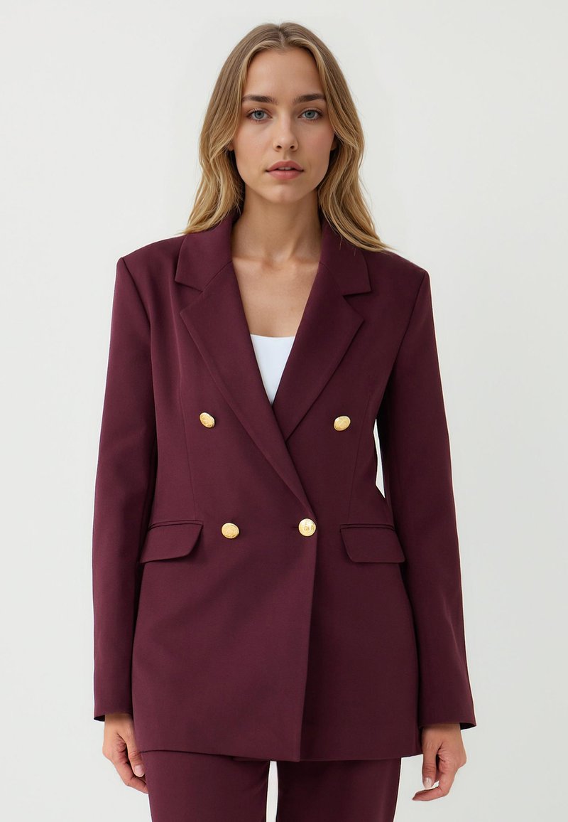 Blazer bordeaux à double boutonnage avec des boutons dorés, revers crantés et poches latérales, fabriqué en tissu lisse avec une coupe structurée.