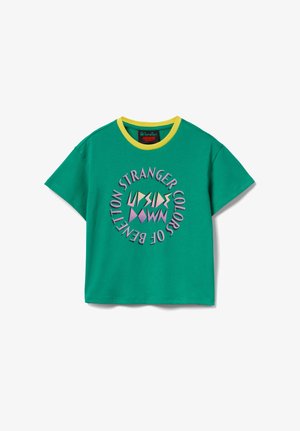 Zielony T-shirt z krótkim rękawem i żółtym kołnierzem, z okrągłym napisem "Stranger Colors of Benetton" otaczającym kolorowe geometryczne kształty na przodzie.