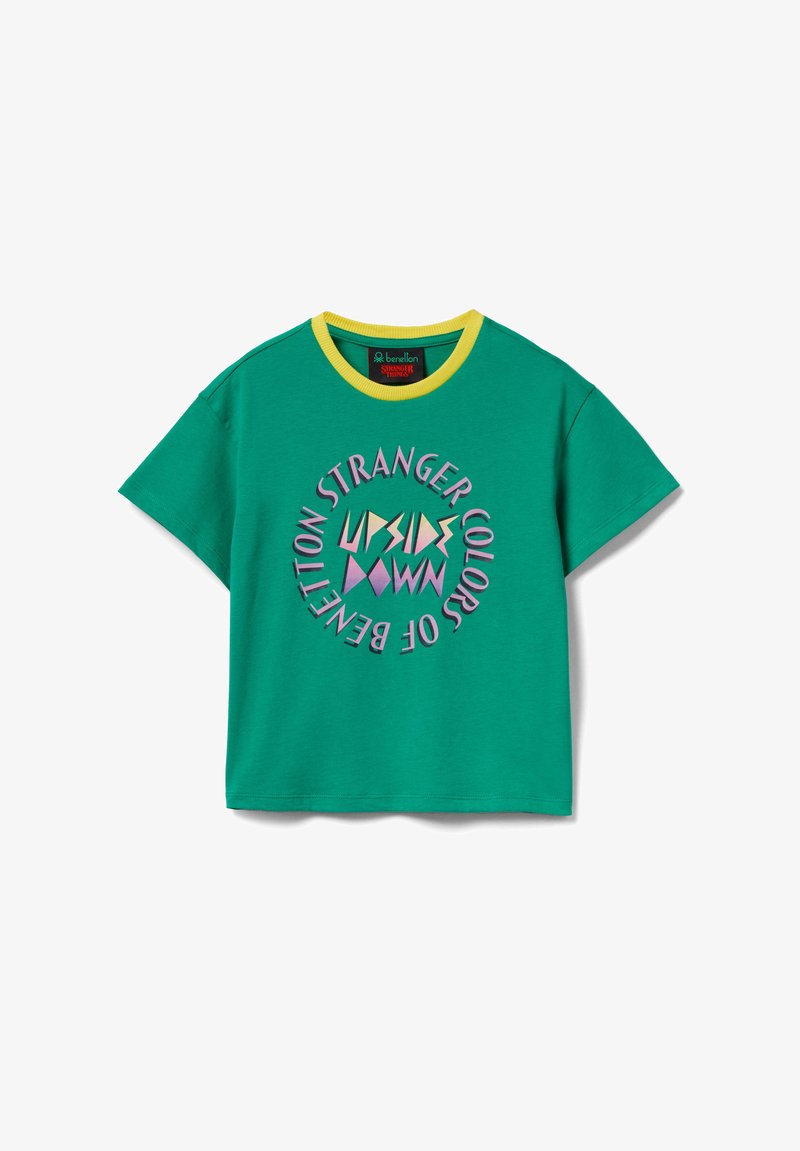 Groen T-shirt met korte mouwen, gele kraag en cirkelvormige tekst "Stranger Colors of Benetton" rondom kleurrijke geometrische vormen aan de voorkant.