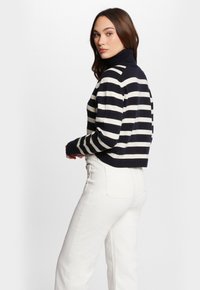 Gestreifter Rollkragenpullover in Marineblau und Creme mit langen Ärmeln, figurnaher Passform und gerippten Bündchen, kombiniert mit weißen hochtaillierten Jeans.