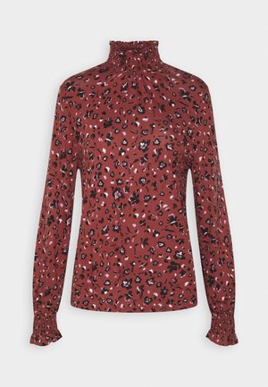 Red long-sleeve top with a high smocked neck, featuring a floral pattern with black and pink accents. Soft, jersey-like material with gathered cuffs.