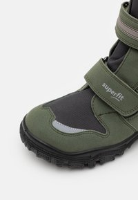 Zelené semišové boty s černou síťovinou a gumovou podrážkou. Obsahují suchý zip a reflexní prvky pro zvýšení viditelnosti.