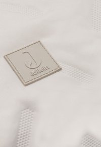 Witte stof met een textuurpatroon, met een grijze rechthoekige logoplaat die het merk "Jollein" en een gestileerde letter "J" in reliëf draagt.