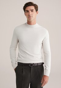 Valge pika varrukaga sviiter kõrge kaelusega, kombineeritud tumedate hallide pükste ja musta naha rihmaga. Pehme tekstuur, keha lähedane disain.