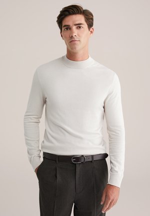 Suéter blanco de manga larga con un cuello alto, combinado con pantalones gris oscuro y un cinturón de cuero negro. Textura suave, diseño ajustado.
