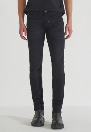 Jean en denim noir avec une coupe slim, design à cinq poches et texture lisse. Dispose d'une fermeture à bouton et à glissière. Associé à des bottes noires.