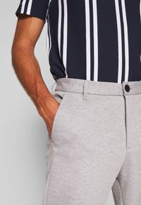Camiseta de rayas navy con rayas verticales blancas, combinada con pantalones grises texturizados que cuentan con un cierre de botón y bolsillos laterales.