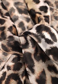 Tessuto con stampa leopardata che presenta sfumature di beige, nero e marrone. Texture morbida con una finitura liscia, piegato in una forma fluida.