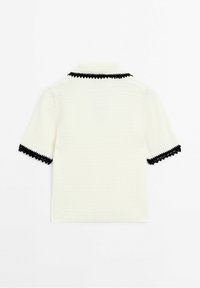 Haut tricoté blanc à manches courtes avec bordure zébrée noire sur le col et les bords des manches, présenté à plat vue de dos.