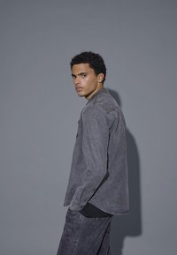 Graues Denim-Hemd mit langen Ärmeln und spitzem Kragen, in lässiger Passform, mit subtiler Textur und einer einzelnen Brusttasche.