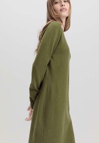 Abito verde oliva a maniche lunghe realizzato in tessuto texturizzato, caratterizzato da una vestibilità comoda e aperture laterali per facilitare i movimenti.