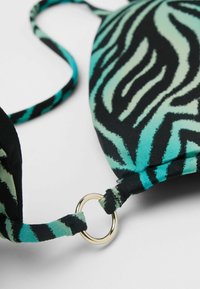 Sostén de bikini a rayas de cebra en negro y verde menta con copas suaves, tirantes ajustables y un detalle en forma de anillo de metal dorado en el tirante.