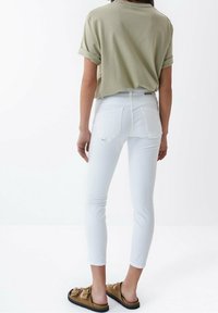 Bílé úzké džíny, olivově zelené zkrácené tričko a hnědé sandály na klínku. Džínovina má hladkou texturu a klasický design s pěti kapsami.