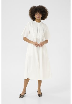 Vestido midi blanco con mangas cortas, botones en la parte delantera y rayas verticales texturizadas. Combinado con tacones de rayas en blanco y negro.