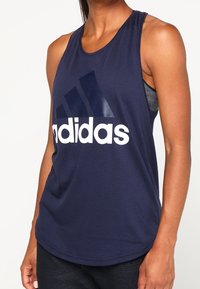 Camiseta sin mangas Adidas de color azul marino, fabricada con un tejido suave y con un escote redondo. Presenta un gran logo blanco en la parte delantera y un diseño de corte relajado.